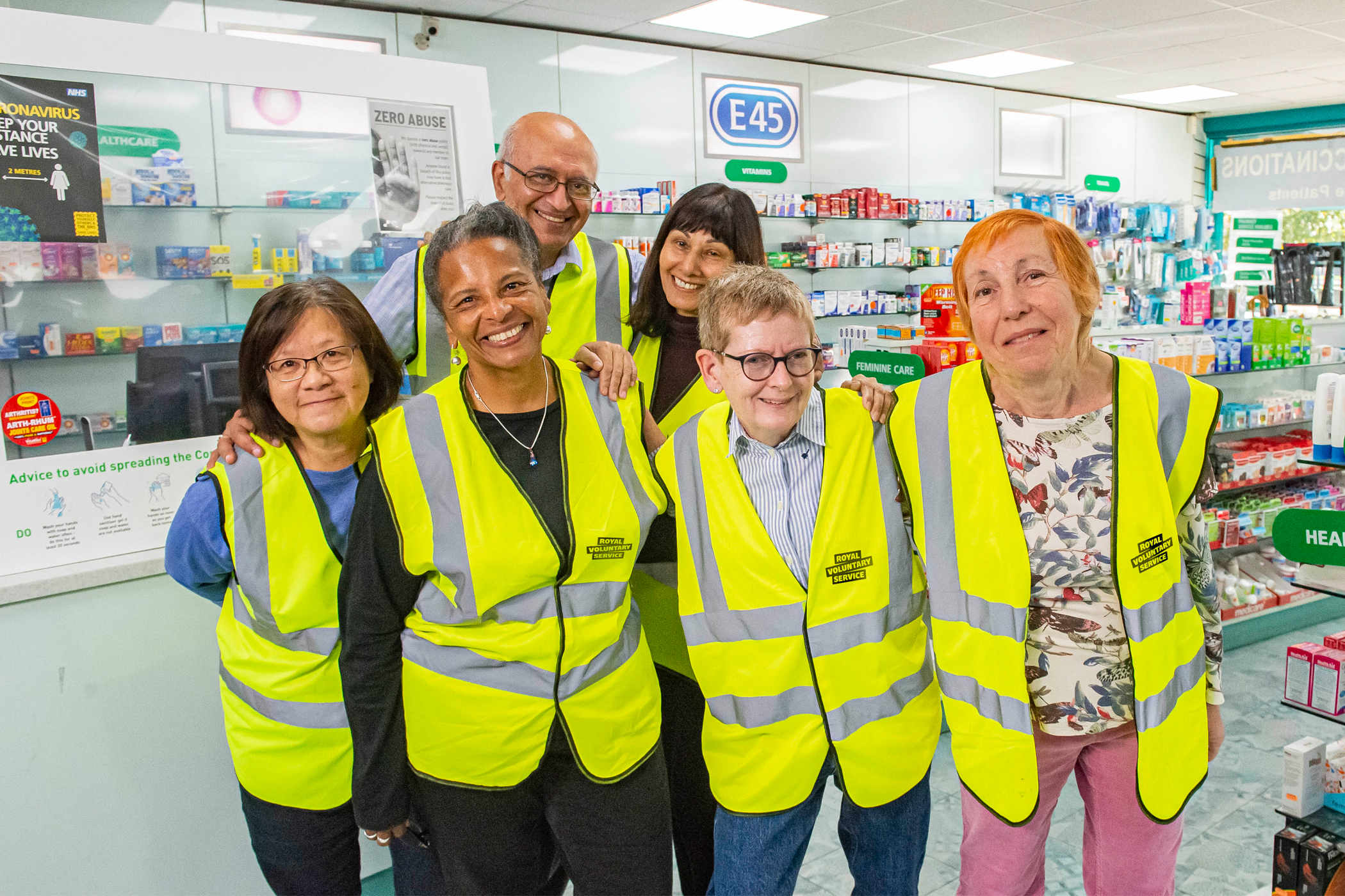 A group of diverse Royal Voluntary Service volunteers in high vis vests at a chemist 