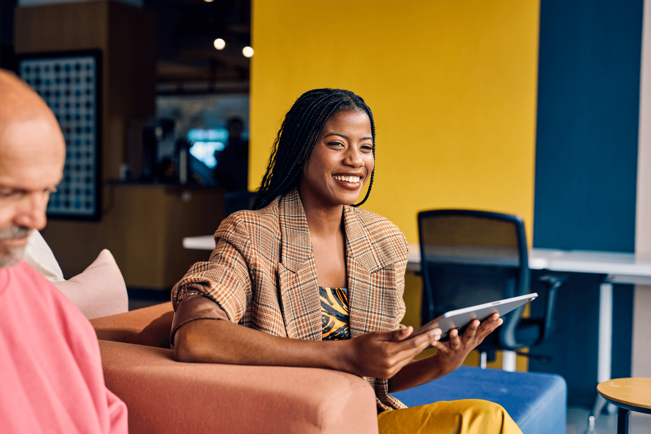 A young woman sat in a business environment smiling and happy whilst using a tablet