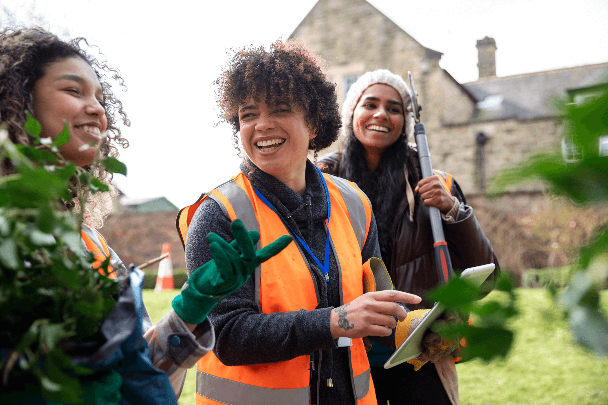 A woman smiling, whilst giving directions to others whilst gardening outside